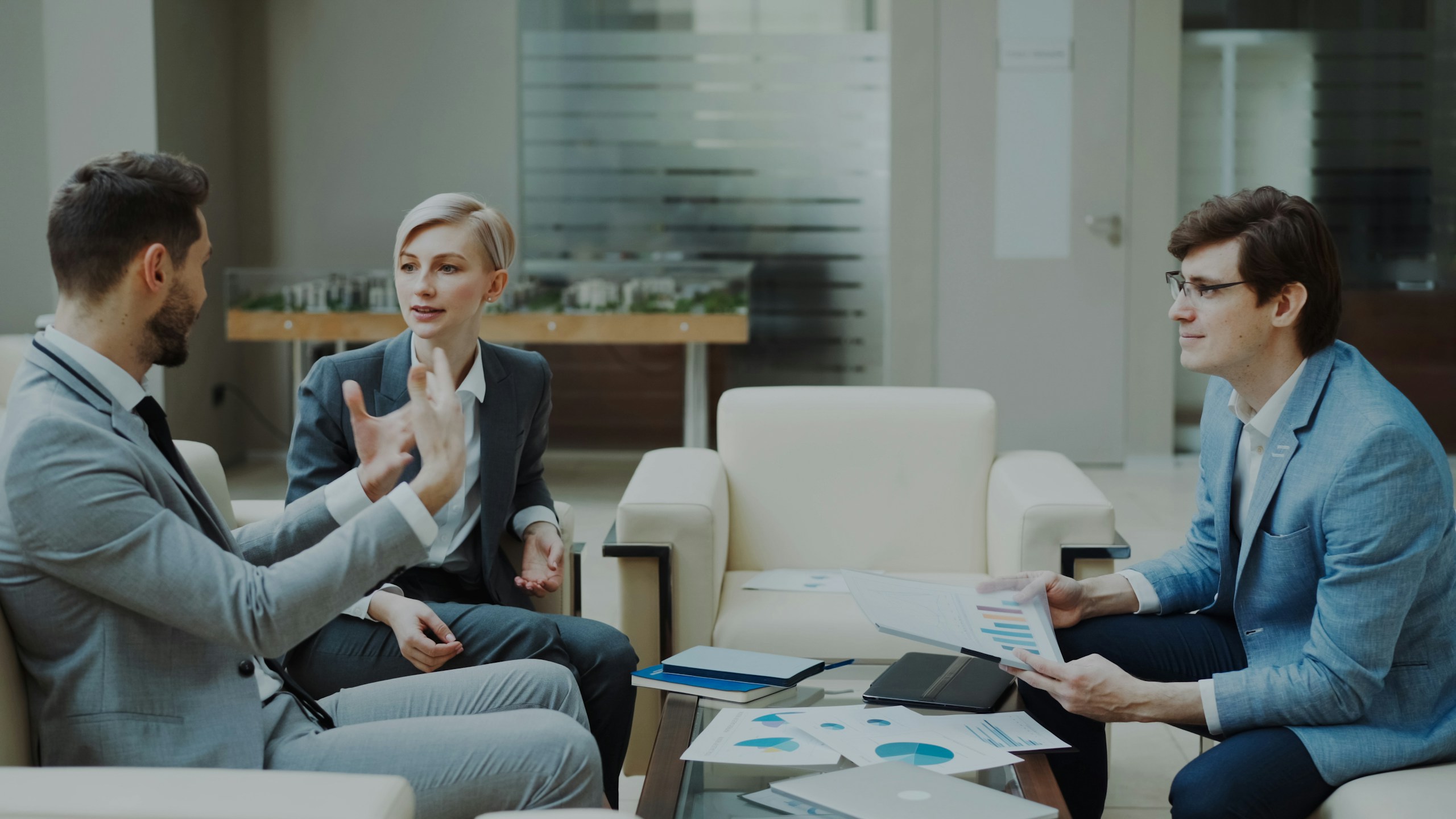 businessman discussing financial reports with female and male business partners sitting on sofa in modern office hall with indoors