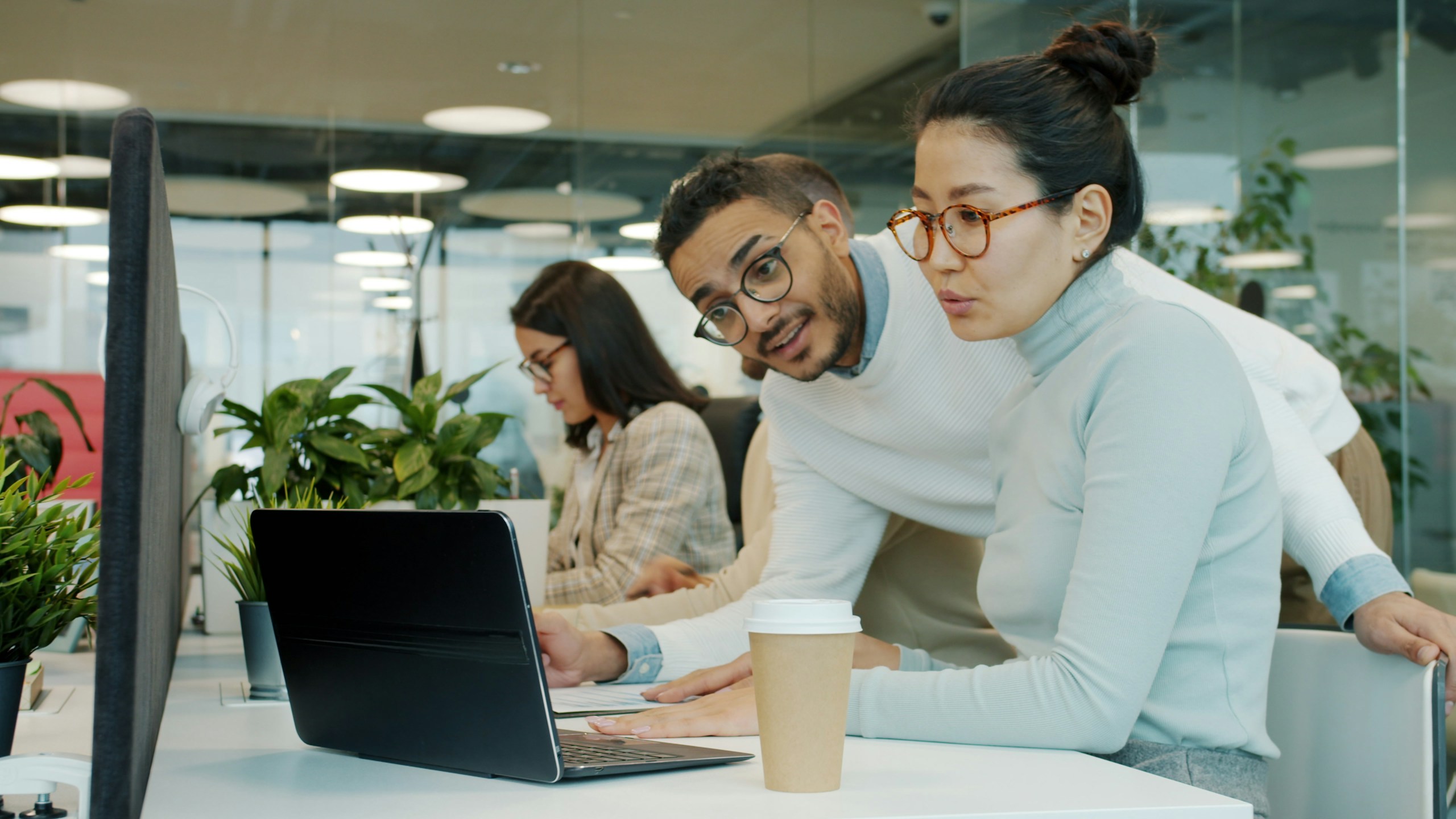 Colleagues Asian woman and Arabian man are talking looking at laptop screen working with computer in shared office. Cooperation and workplace concept.