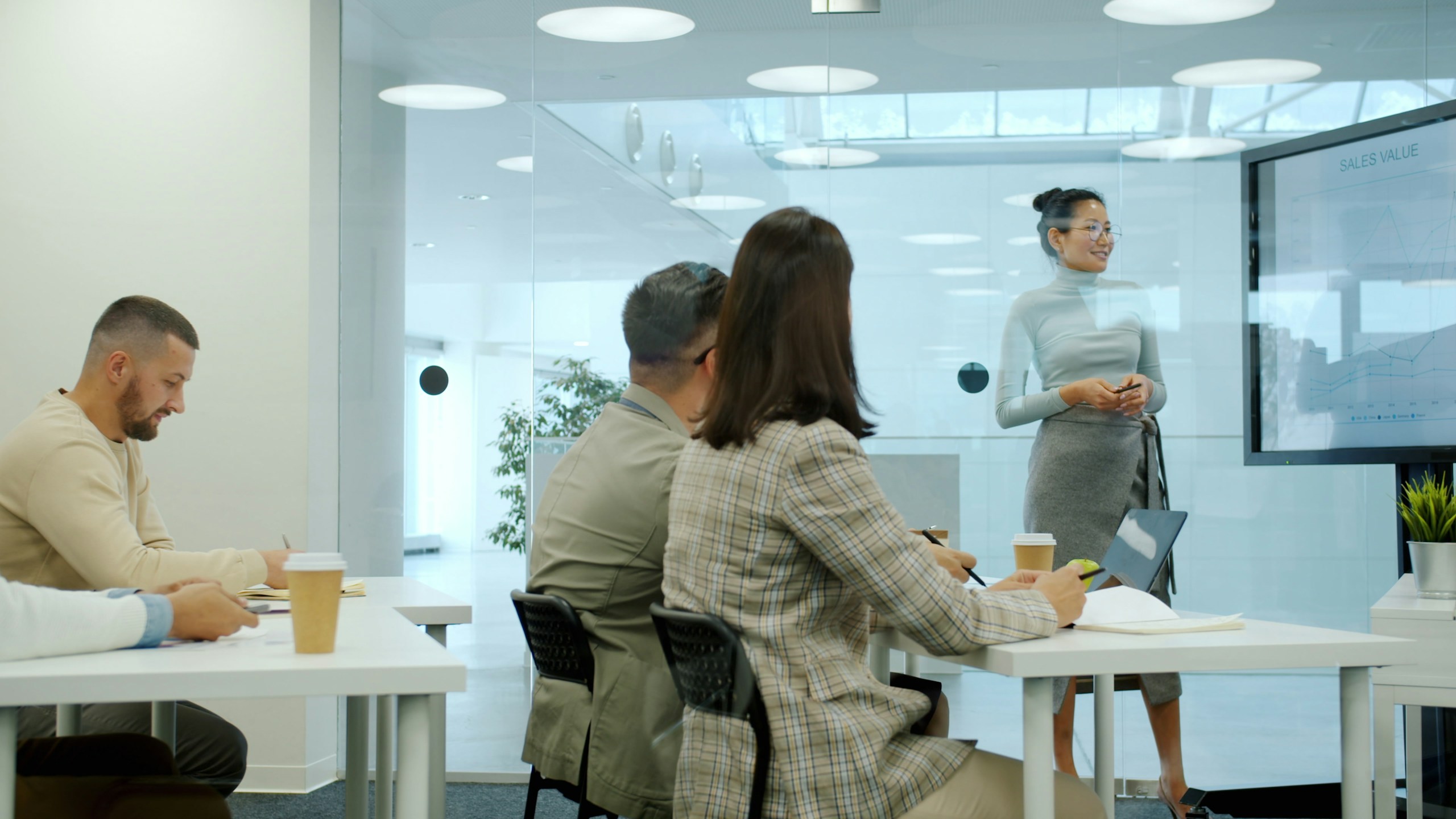 Female boss Asian lady is speaking to group of employees in conference room using digital board teaching people about marketing and business.